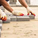 workers lay paving tiles, construction of brick pavement, men's hands in gloves, close up architecture background